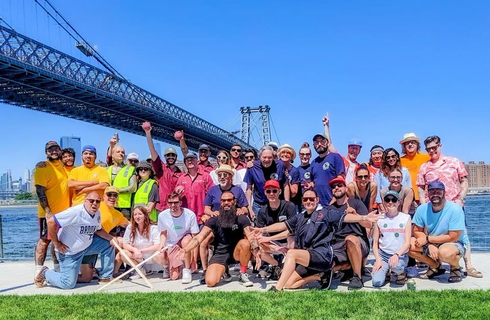 Bocce for Bus participants gathered at Domino Park under the Williamsburg Bridge
